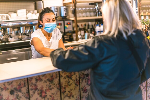 Fotosession mit einer Kellnerin mit einer Gesichtsmaske in einer Bar. Einen Kaffee an einen Kunden liefern