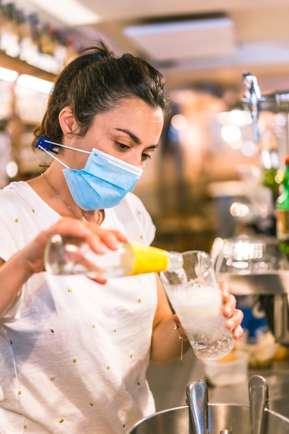 Fotosession mit einer kellnerin mit einer gesichtsmaske in einer bar. gin tonic in ein glas geben