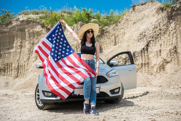 Fotoshooting einer charmanten Dame mit der USA-Flagge neben dem Auto in einem Sandsteinbruch im Sommer