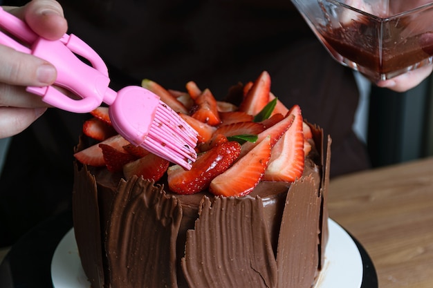 Fotoshooting mit Schokoladenkuchen, der dekoriert wird. Schokoladenkuchen bedeckt mit Erdbeeren, frischen Basilikumblättern, Brombeermarmelade und Schokoladenplatten herum.