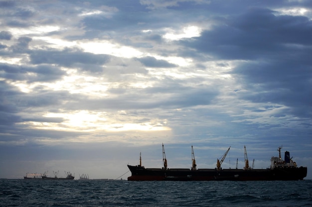 Frachter-Frachtschiff, das im Meer schwimmt, Warteschlange, Güter während der regnerischen Sturmabend-Dämmerungszeit zwischen Koh Loy und der Insel Ko Sichang in der Stadt Sriracha in Chonburi, Thailand, transportiert