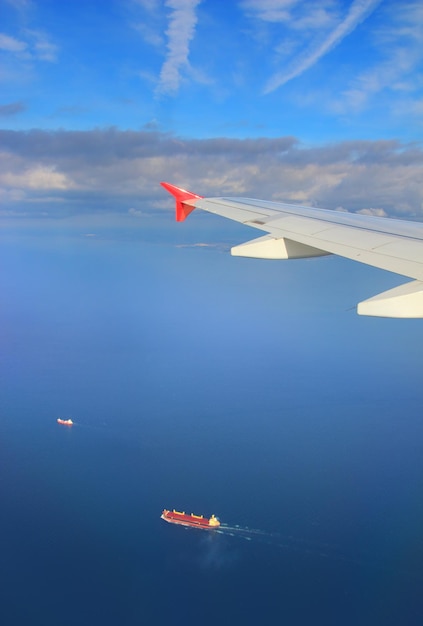 Frachtschiffe unter dem Flügel eines fliegenden Flugzeugs