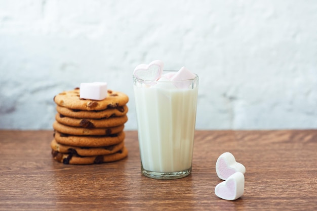 Fragantes y sabrosas galletas caseras con pasas de malvavisco en forma de corazón y un vaso de leche fresca sobre la mesa