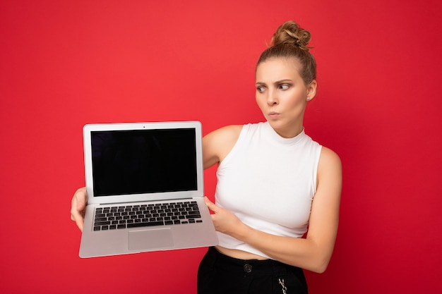 Fragen Sie die blonde junge Frau mit den gesammelten Haaren und den Zweifeln, die auf die Netbook-Tastatur schauen