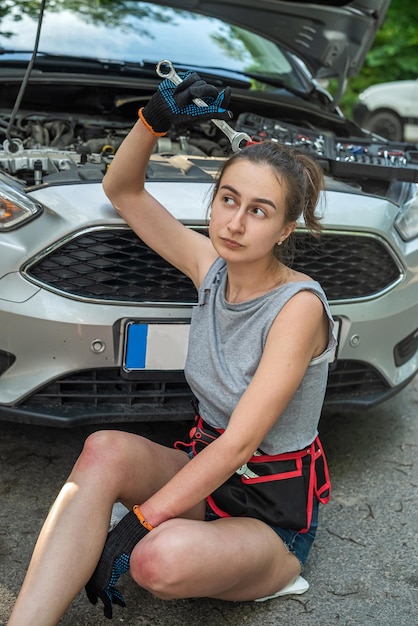 Foto fragile schöne mädchen mit öl verschmiert mit vielen werkzeugen in ihren händen repariert das auto das konzept der autoreparatur auf der straße auto-konzept auf der straße