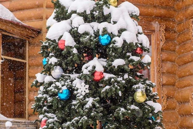 Fragment des Weihnachtsbaumes mit bunten Kugeln auf den Zweigen auf der Straße im Hintergrund eines Holzhauses