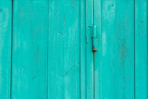 Un fragmento de una antigua puerta de madera de color azul o turquesa sobre bisagras oxidadas.