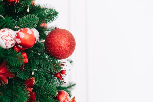 Un fragmento de un árbol de Navidad decorado con bolas rojas sobre una pared blanca de fondo, concepto de Navidad y Año Nuevo