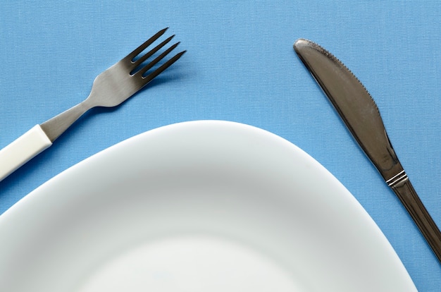 Fragmento de prato vazio na toalha de mesa azul com garfo e faca