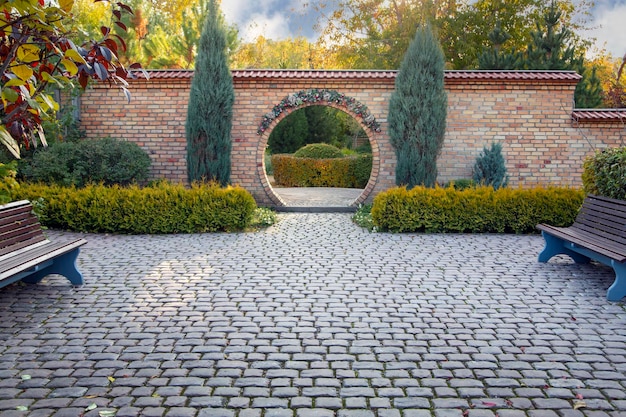 Un fragmento de diseño paisajístico en un parque otoñal con árboles y arbustos bellamente recortados, un arco y un callejón pavimentado