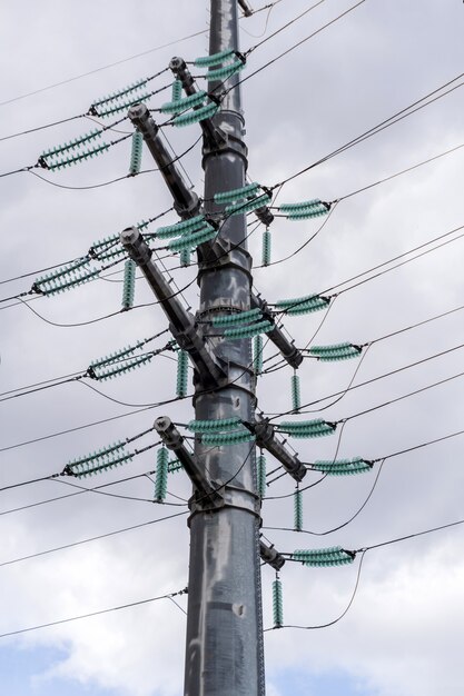 Fragmento de una enorme torre de líneas eléctricas con aisladores y cables verdes contra un cielo nublado