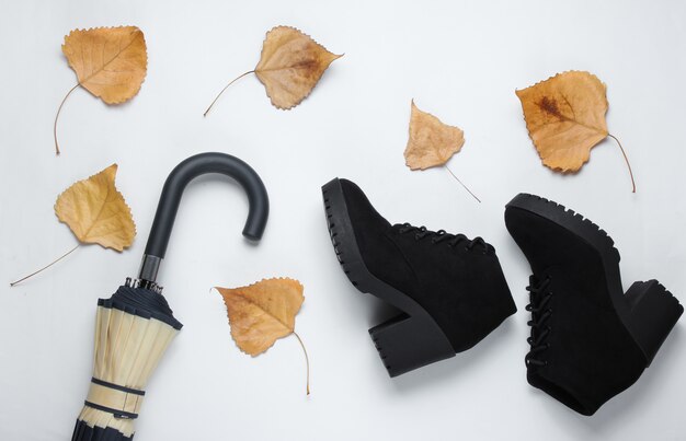 Fragmento de gancho de paraguas, botas y hojas caídas en la mesa blanca. Vista superior. Accesorios de otoño Lay Flat