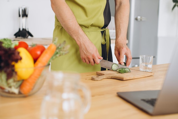 Fragmento de un hombre haciendo una ensalada de verduras frescas en la cocina de casa