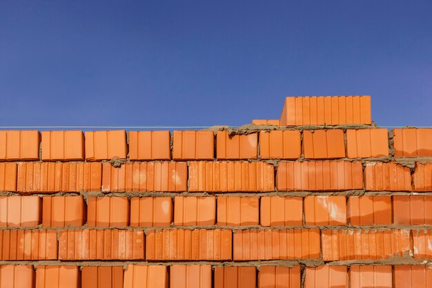 Fragmento de una pared de ladrillos sobre un fondo de cielo azul Pared de ladrillo y grúa torre detrás