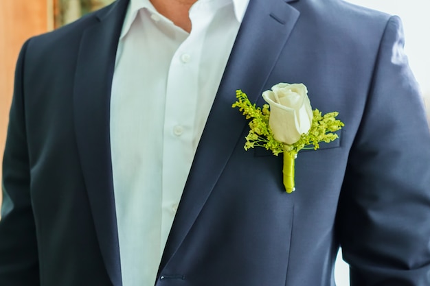 Un fragmento del torso del hombre del novio en una chaqueta azul y una camisa blanca con un ramo de rosas blancas.