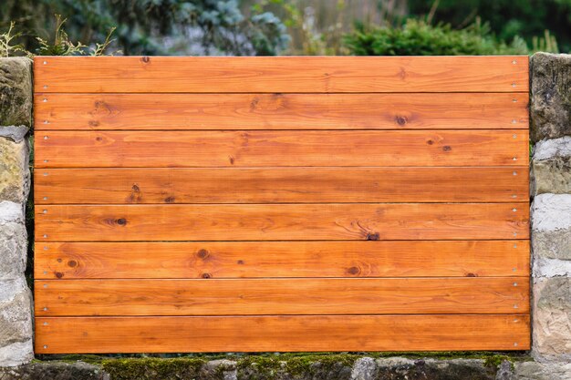 Foto fragmento de valla de madera con tablones horizontales y columnas de piedra natural.