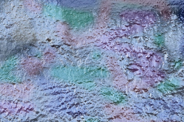 Fragmentos de um muro de concreto pintado com tinta prateada metálica multicolorida.