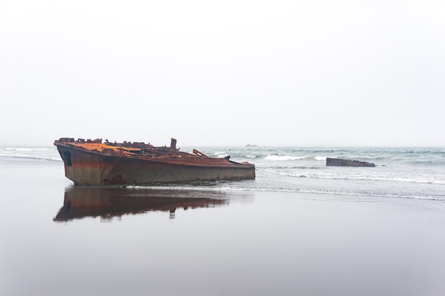 Fragmentos oxidados del naufragio de un barco arrastrado a tierra contra un paisaje marino brumoso