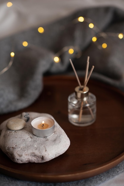 Fragrância doméstica líquida com vela perfumada queimando na bandeja de pedra sobre luzes de natal brilhantes em casa close-up Atmosfera hygge aconchegante com luz de velas