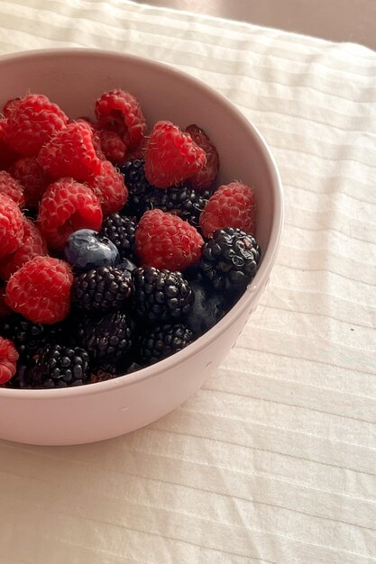 Framboesas amoras e mirtilos em um copo rosa closeup o conceito de alimentação saudável o conceito de verão imagem vertical fechar