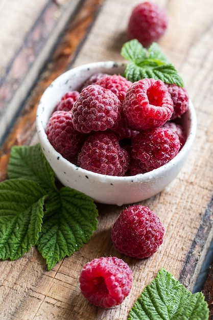 Foto framboesas frescas suculentas com folhas verdes em um prato sobre uma mesa de madeira. baga saudável, alimentos orgânicos, antioxidante