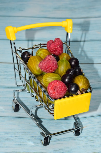 Framboesas, groselhas e groselhas estão empilhadas em um pequeno carrinho de compras de brinquedo amarelo. Close fotografado