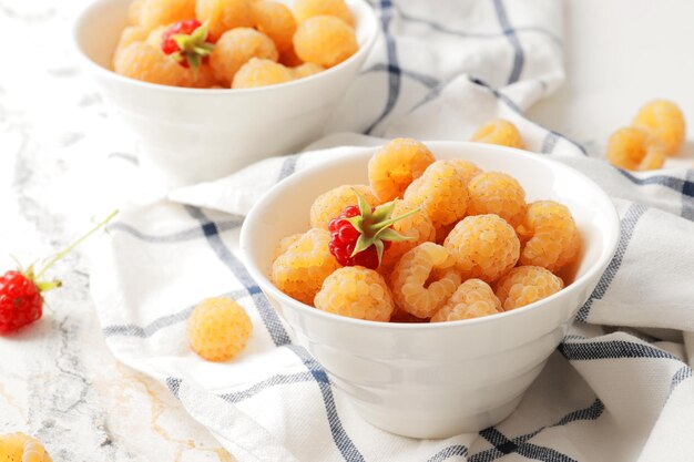 Foto frambuesas amarillas maduras en un bol con un paño de cocina sobre un fondo de mármol un bol lleno de frambuesas ingredientes de postre