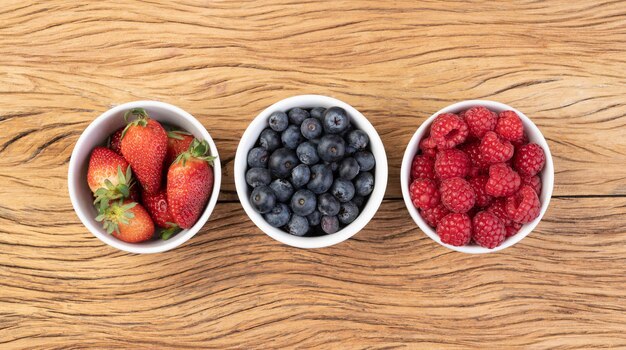 Frambuesas fresas y arándanos en tazones sobre mesa de madera