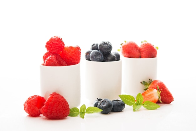 Frambuesas frescas del jardín en un vaso blanco sobre blanco