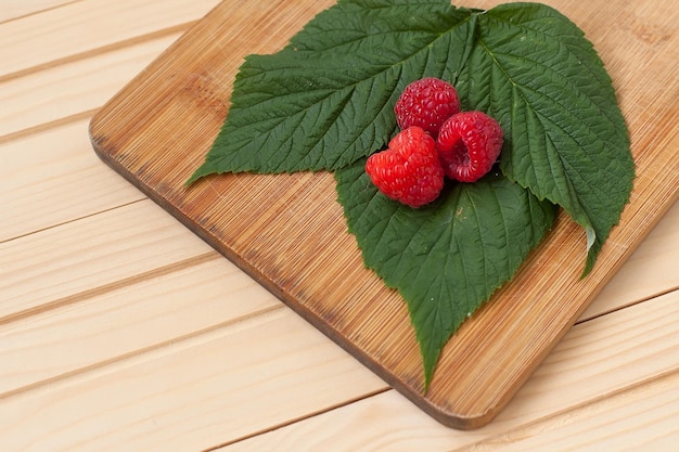 Frambuesas frescas rojas sobre fondo blanco de madera rústica Cuenco con bayas orgánicas maduras naturales con pedúnculos y hojas verdes sobre una mesa de madera con espacio para copiar