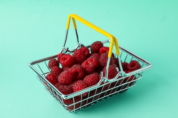 Frambuesas jugosas rojas en una cesta de la compra sobre un fondo de mentol.