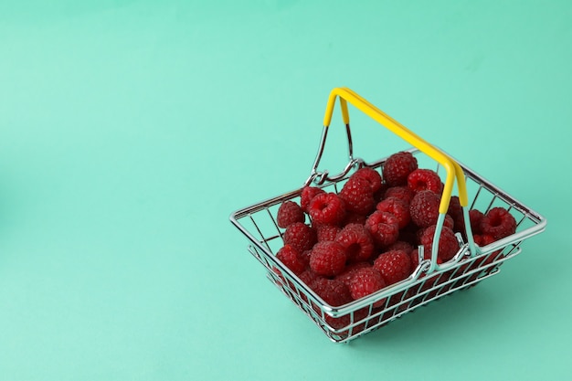 Frambuesas jugosas rojas en una cesta de la compra sobre un fondo de mentol.