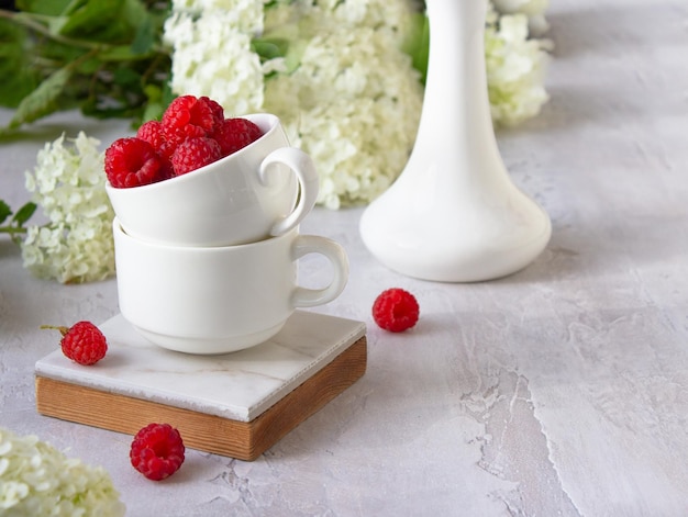 Frambuesas rojas y un ramo de flores blancas del jardín de verano sobre la mesa