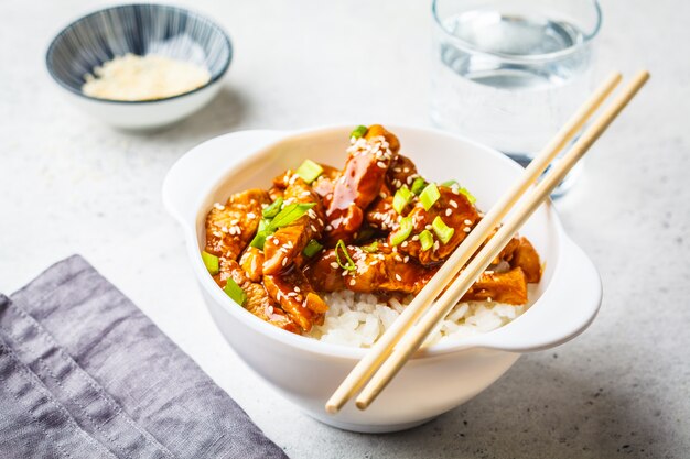 Frango asiático do teriyaki com arroz, sésamo e cebolas verdes na bacia branca.