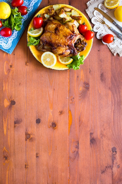 Frango assado caseiro com limão e batatas em uma superfície de madeira