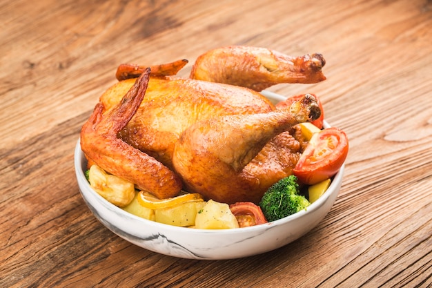 Frango assado com legumes na mesa de madeira