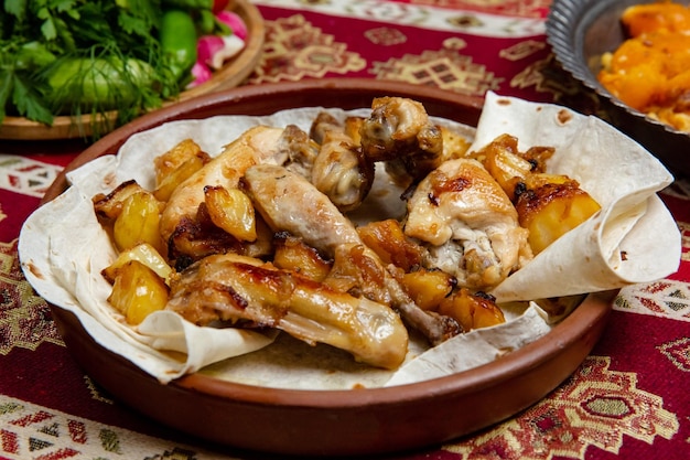 Frango assado em pedaços com batatas e cebola em um prato de barro