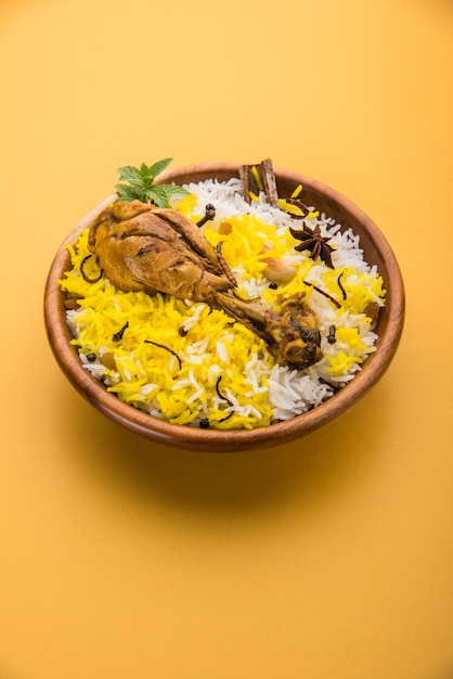 Frango Biryani autêntico servido em uma tigela ou prato sobre fundo colorido ou de madeira. É uma receita deliciosa de arroz Basmati misturado com frango marinado picante servido com salada. Foco seletivo