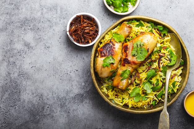 Frango biryani, prato tradicional da culinária indiana, com arroz basmati, cebola frita, coentro fresco em uma tigela sobre fundo cinza de pedra rústica. refeição indiana autêntica, vista de cima, close-up, espaço para texto