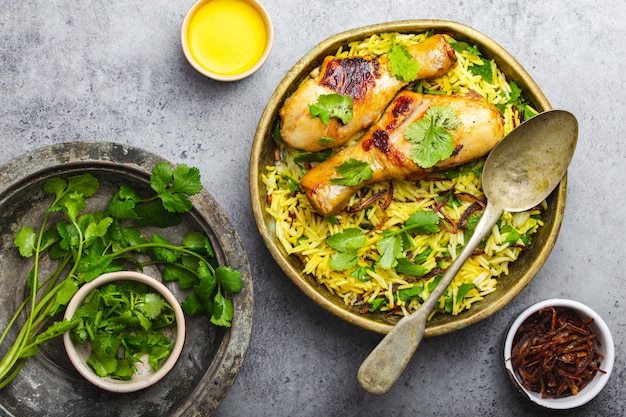 Frango Biryani, prato tradicional da culinária indiana, com arroz basmati, cebola frita, coentro fresco em uma tigela sobre fundo cinza de pedra rústica. Refeição indiana autêntica, vista de cima, close-up