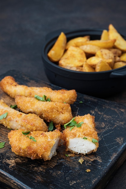 Frango crocante e batatas na mesa escura