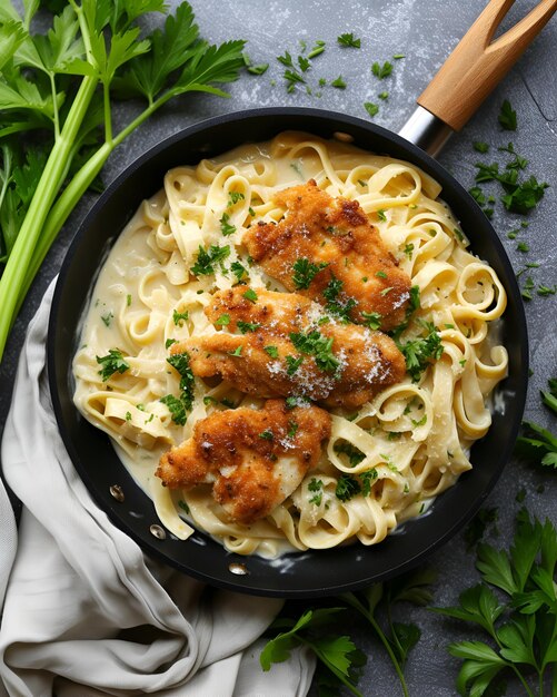 Foto frango crocante fettuccine alfredo na panela preta há folhas de azeitona e pano ao redor da panela