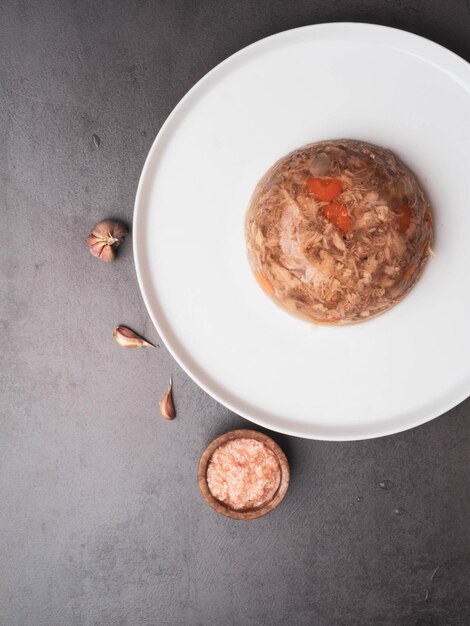 Frango de carne de porco gelatinosa com cenoura e alho em um prato com mostarda picante em um fundo de concreto