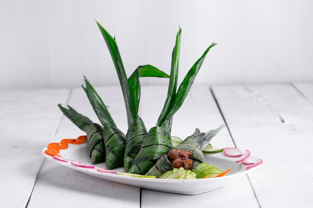 Frango embrulhado em folha de palmeira, lindamente colocado em um prato de cerâmica branca
