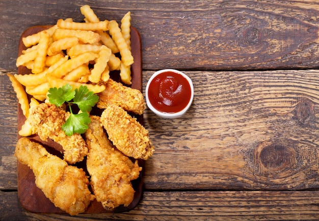 Frango frito e batatas fritas em uma mesa de madeira, vista superior