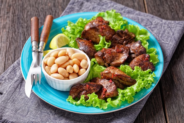 Frango Fry Fry Kaleji Fry servido em folhas de alface com feijão manteiga e fatias de limão em um prato azul em uma mesa de madeira escura cozinha indiana