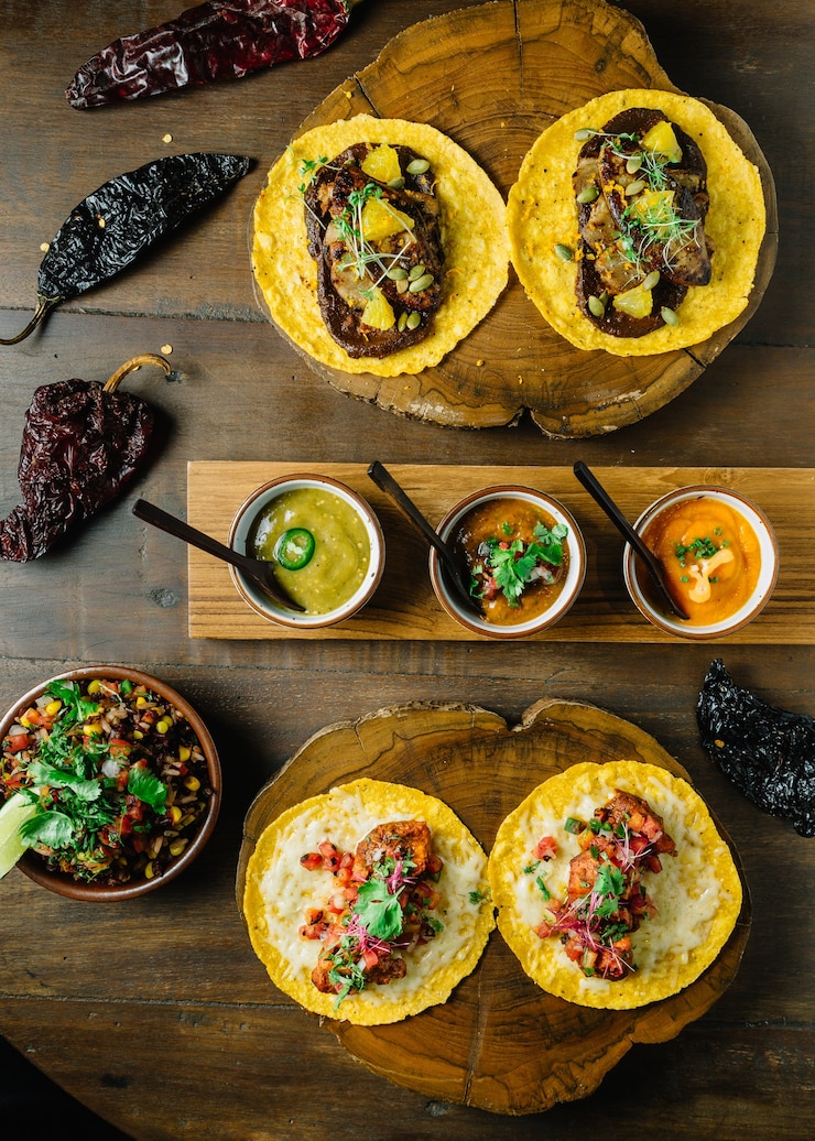 Foto frango grelhado e foie gras tacos servido na tábua de madeira com molhos diferentes.