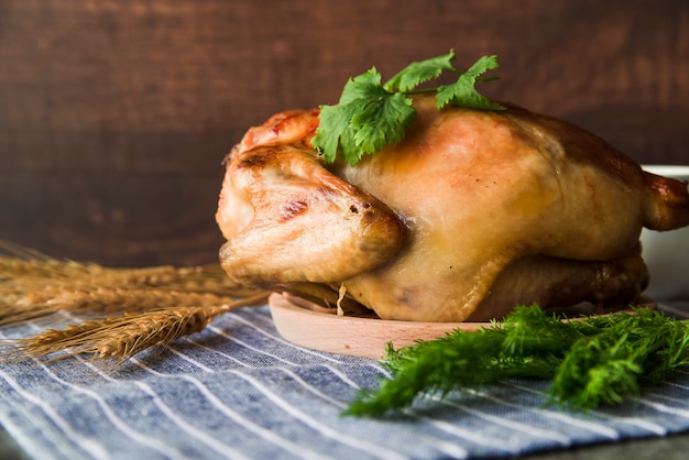 Foto frango guarnecido em placa de madeira com espigas de trigo e endro