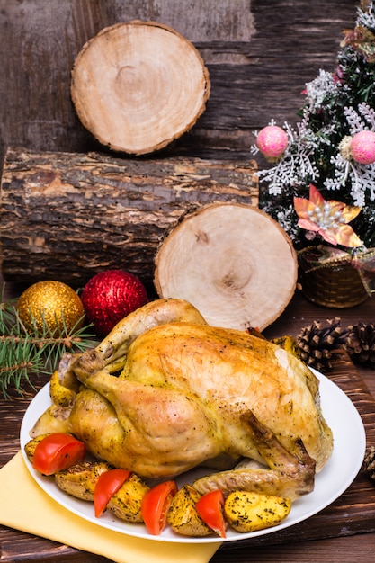 Frango inteiro assado com um enfeite de batatas e tomates em um prato, decoração de natal