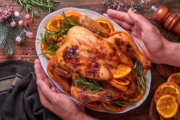 Frango inteiro assado ou assado com alecrim e laranjas, caseiro para o tradicional jantar de natal em família em uma velha mesa rústica de madeira. vista superior com espaço de cópia.